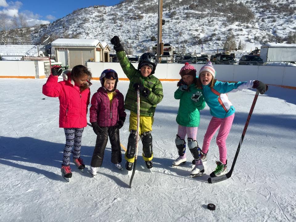 Five children on an ice rink with hockey sticks