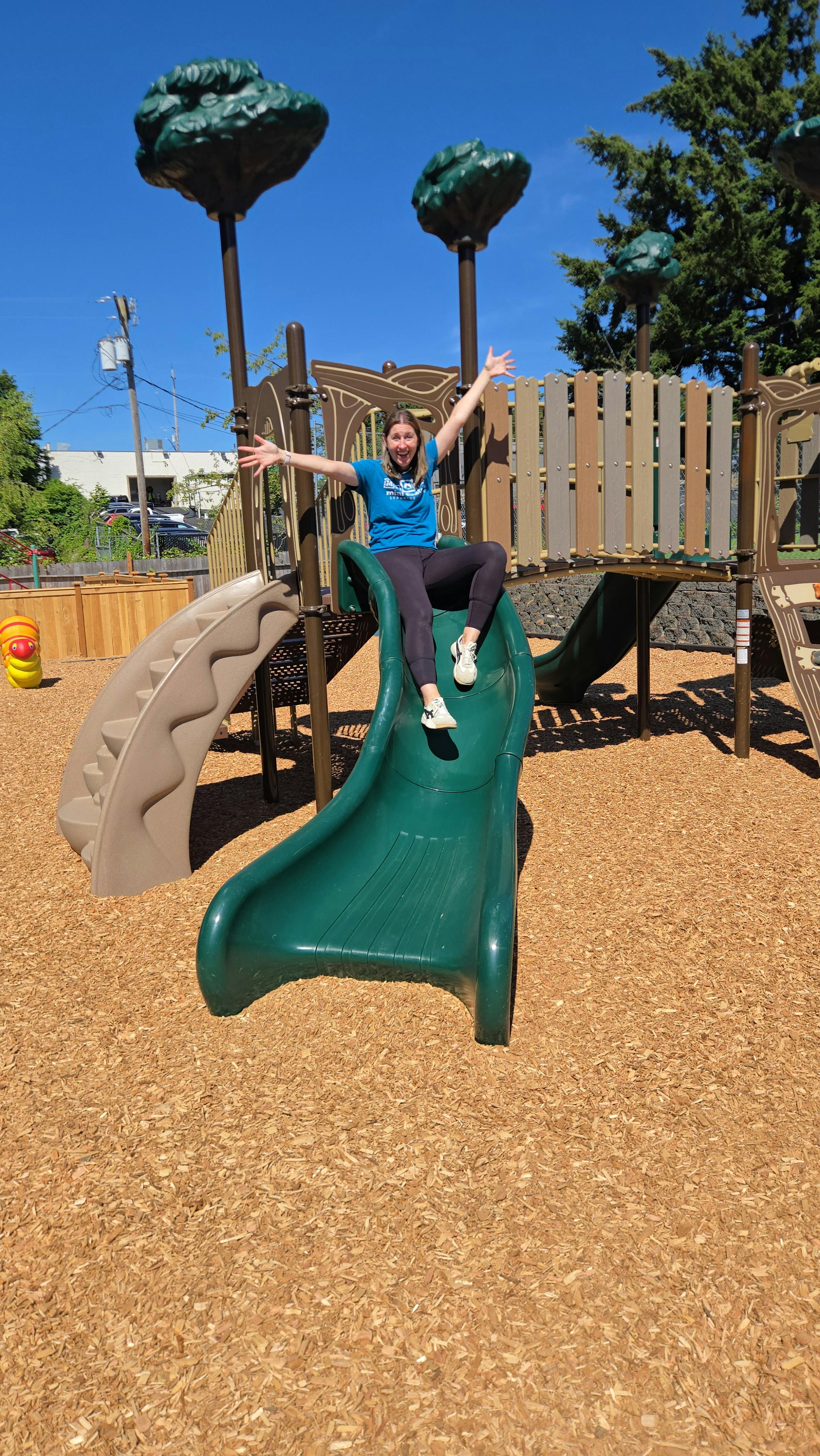 Person sitting on a green slide with arms outstretched on a playground