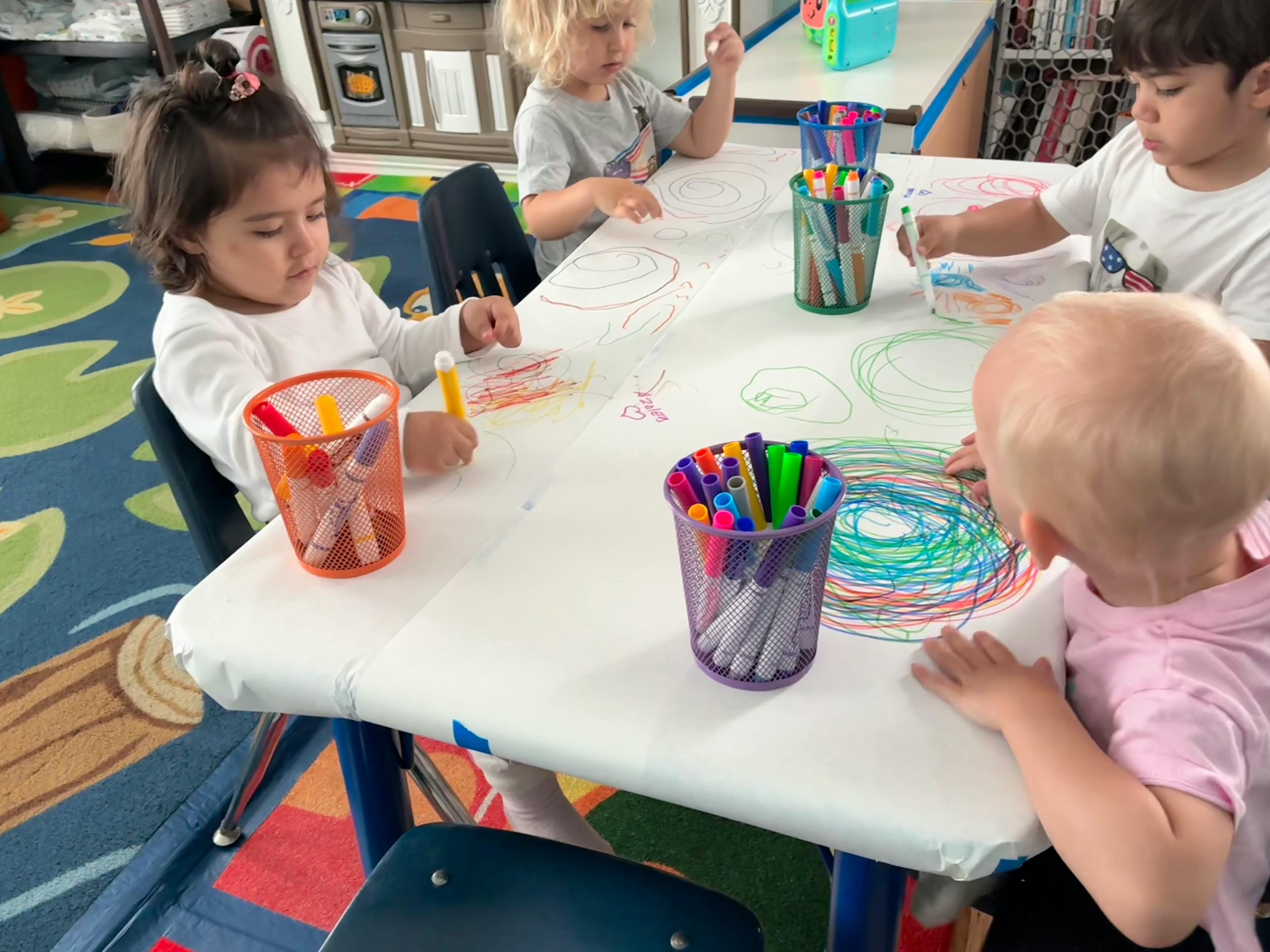 Group of children drawing with markers on a paper-covered table