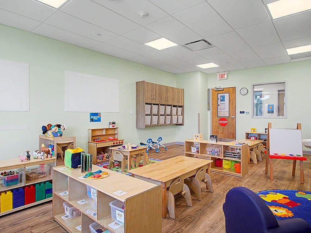 Classroom with small wooden tables and shelves filled with toys and art supplies