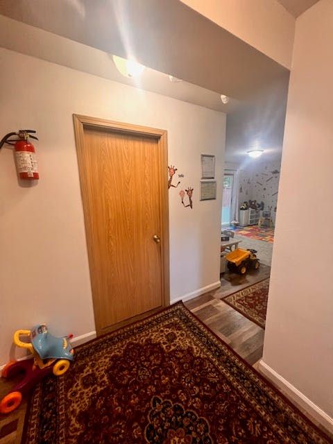 Hallway with a closed door, fire extinguisher, and toys on a rug