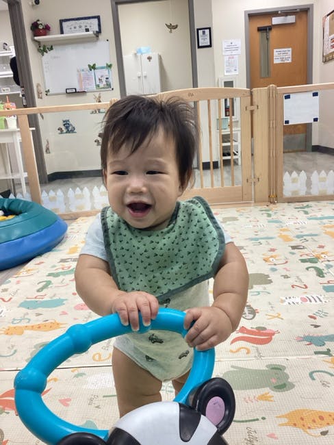Child in a bib holding a blue toy walker