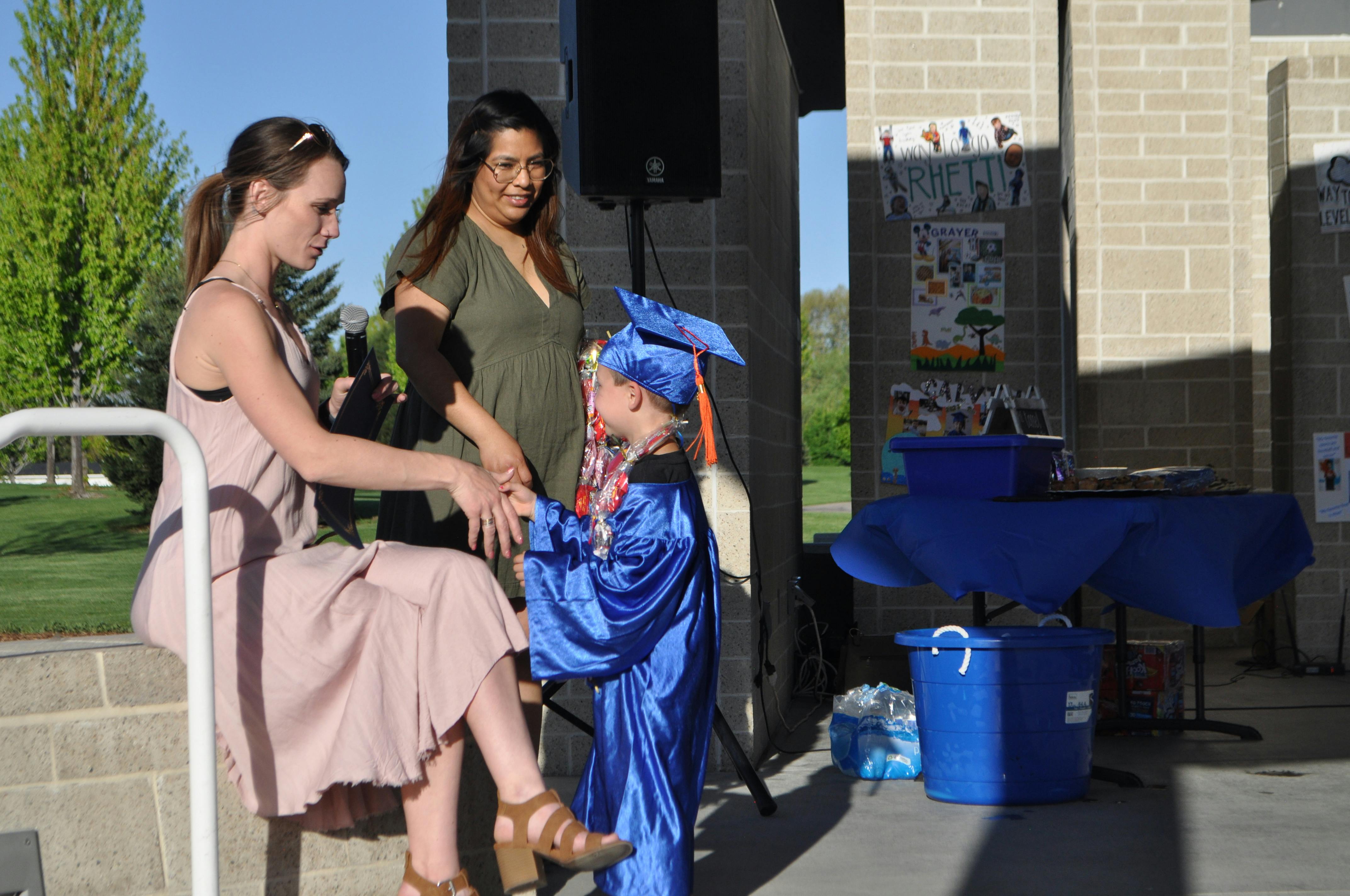 Child in blue graduation gown and cap with two adults