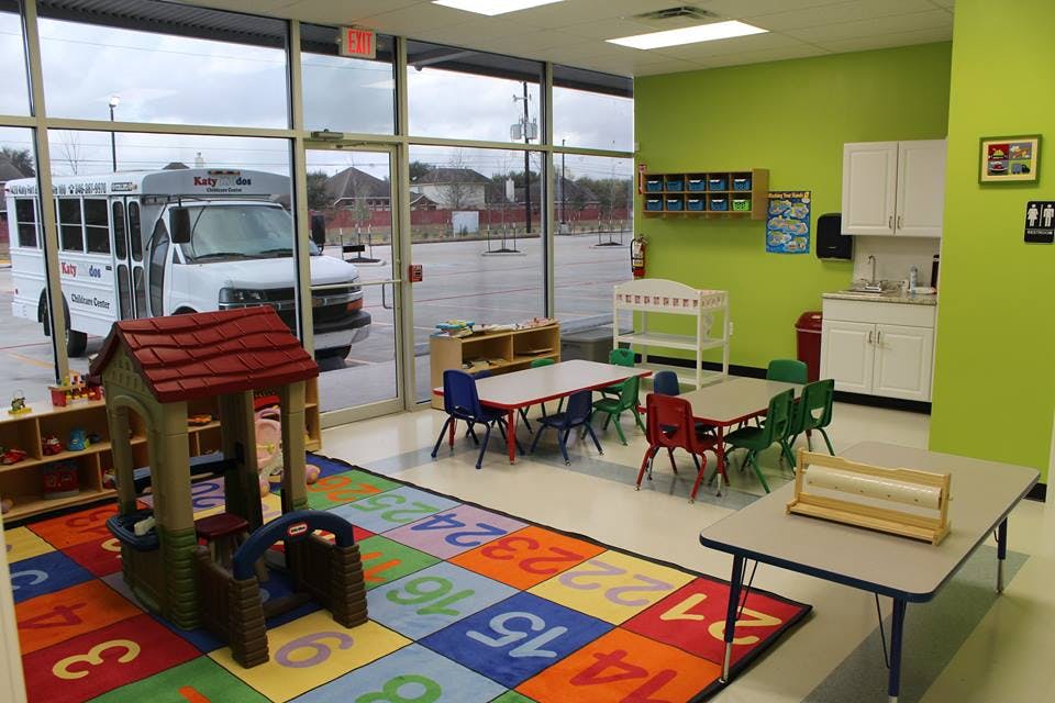 Playroom with small tables and chairs, a playhouse, and a colorful number rug