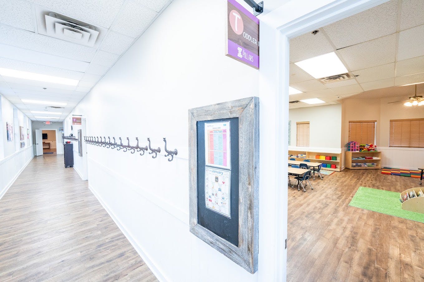 Hallway leading into a toddler classroom with coat hooks and a sign