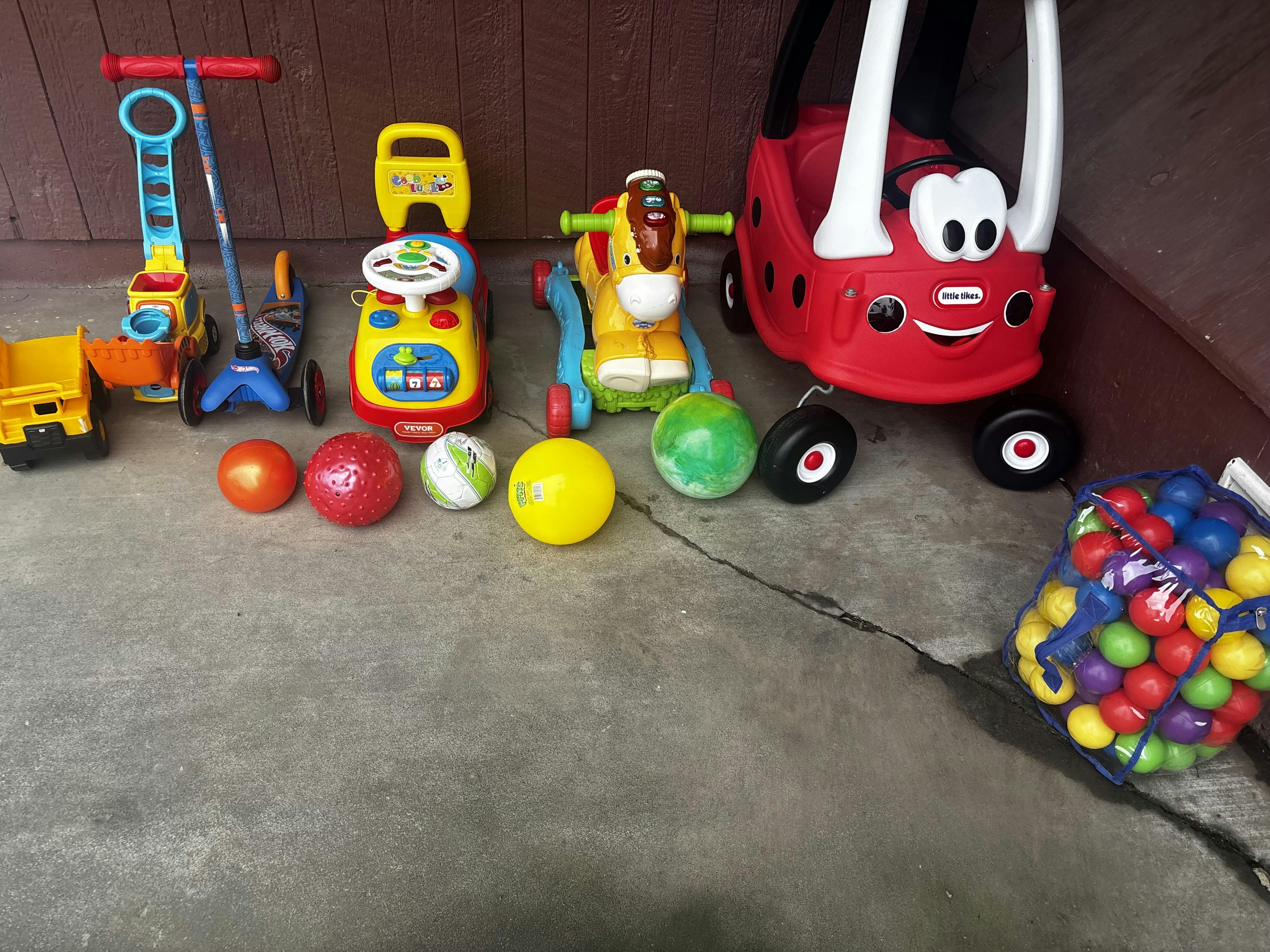 Children's toys including riding vehicles, scooters, and balls on a concrete surface