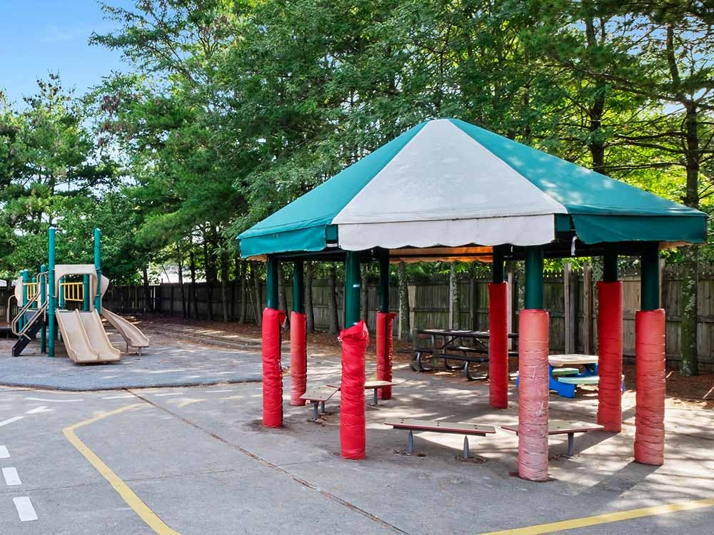Playground area with a canopy covering picnic tables and a slide structure