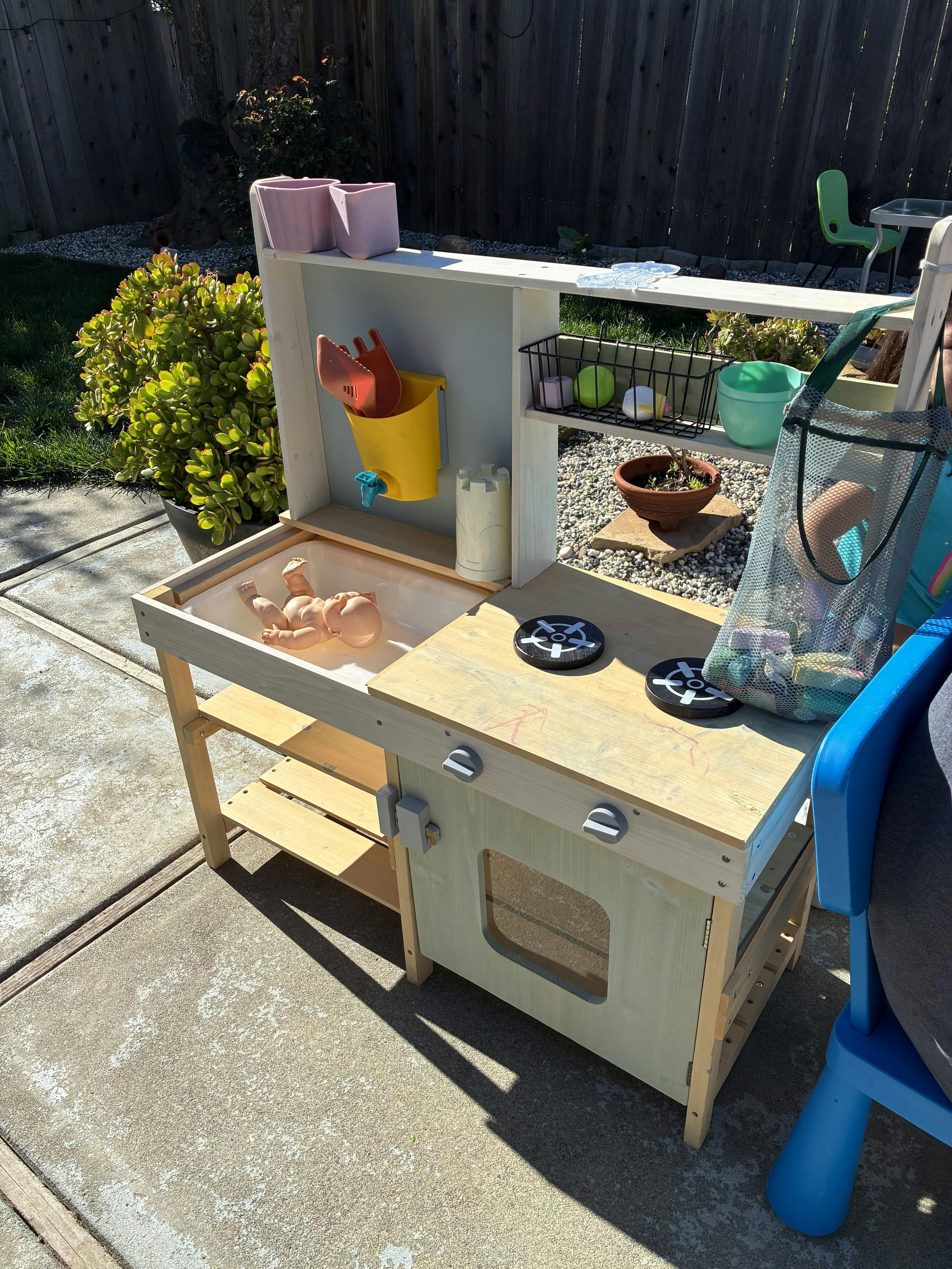Doll in a mud kitchen with gardening tools