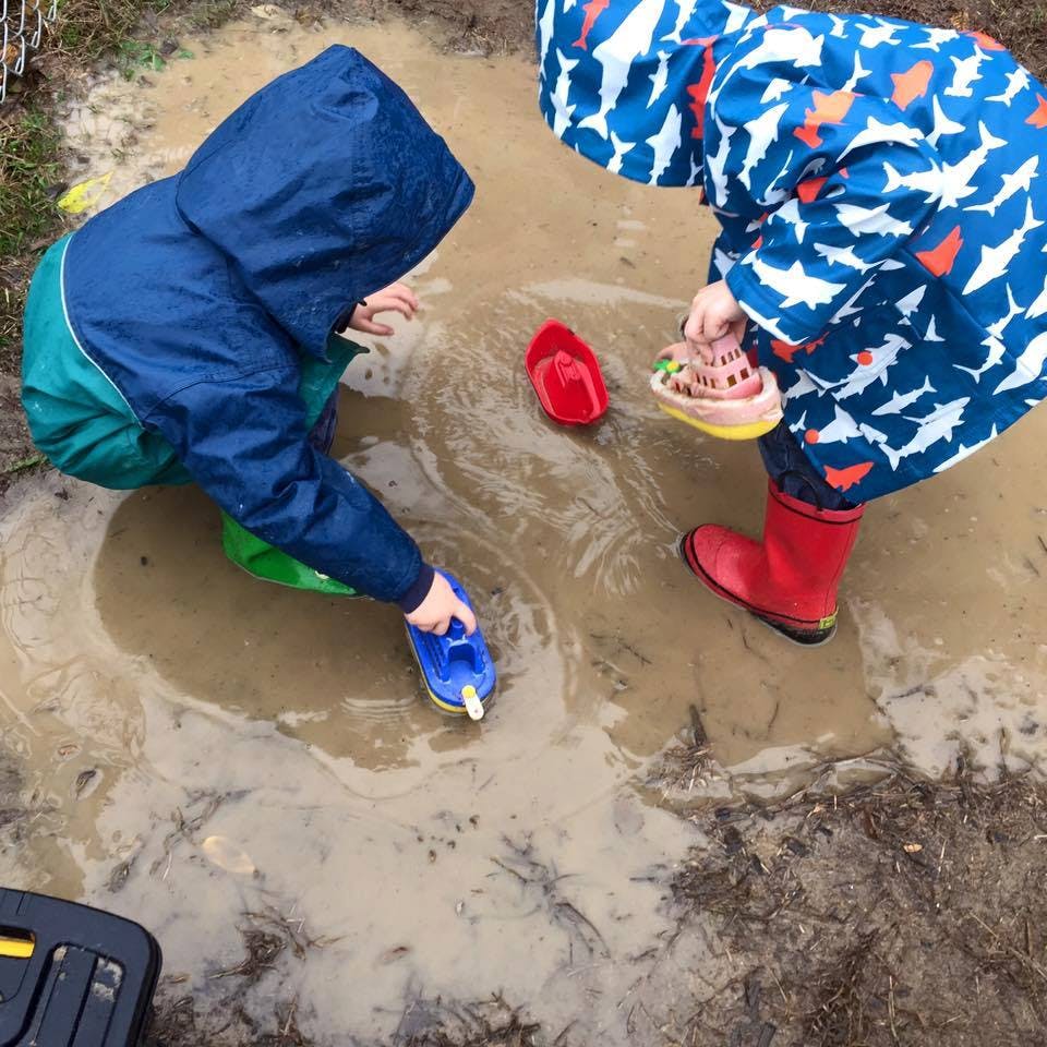 Two children playing with toys in a muddy puddle