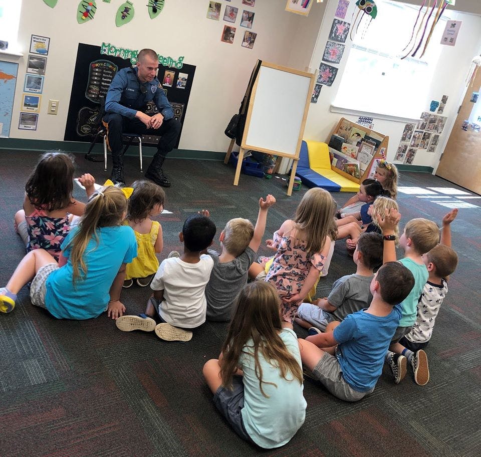 Adult in uniform sitting on a chair with children sitting on the floor around them