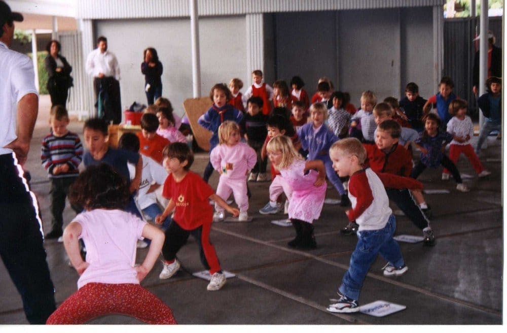 Many children exercising indoors with an adult in a large room