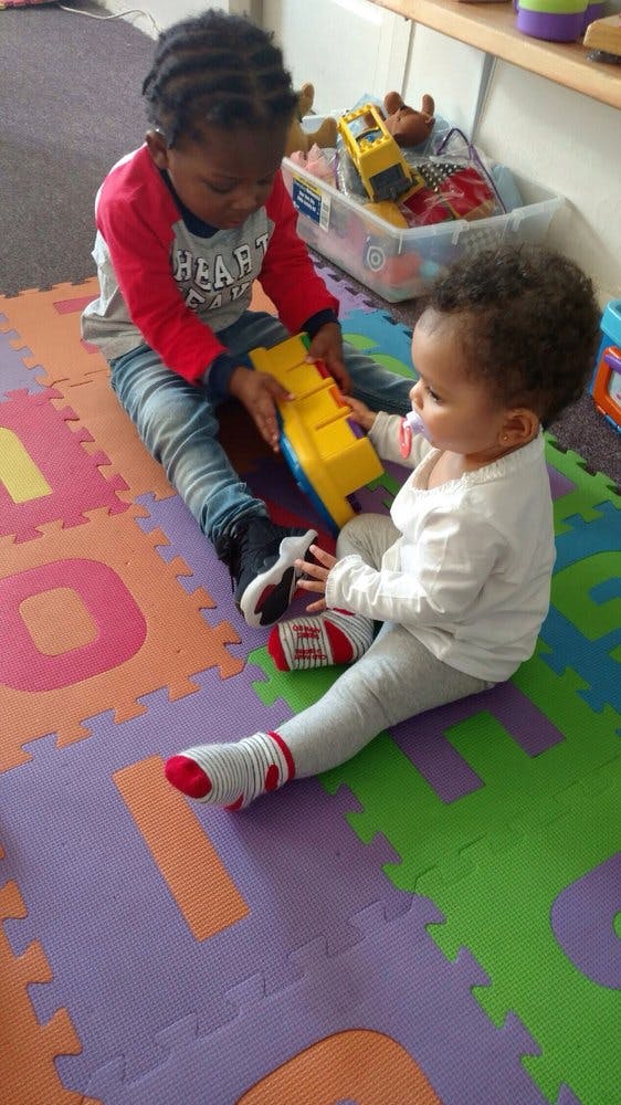 Two children playing with a toy on a colorful mat