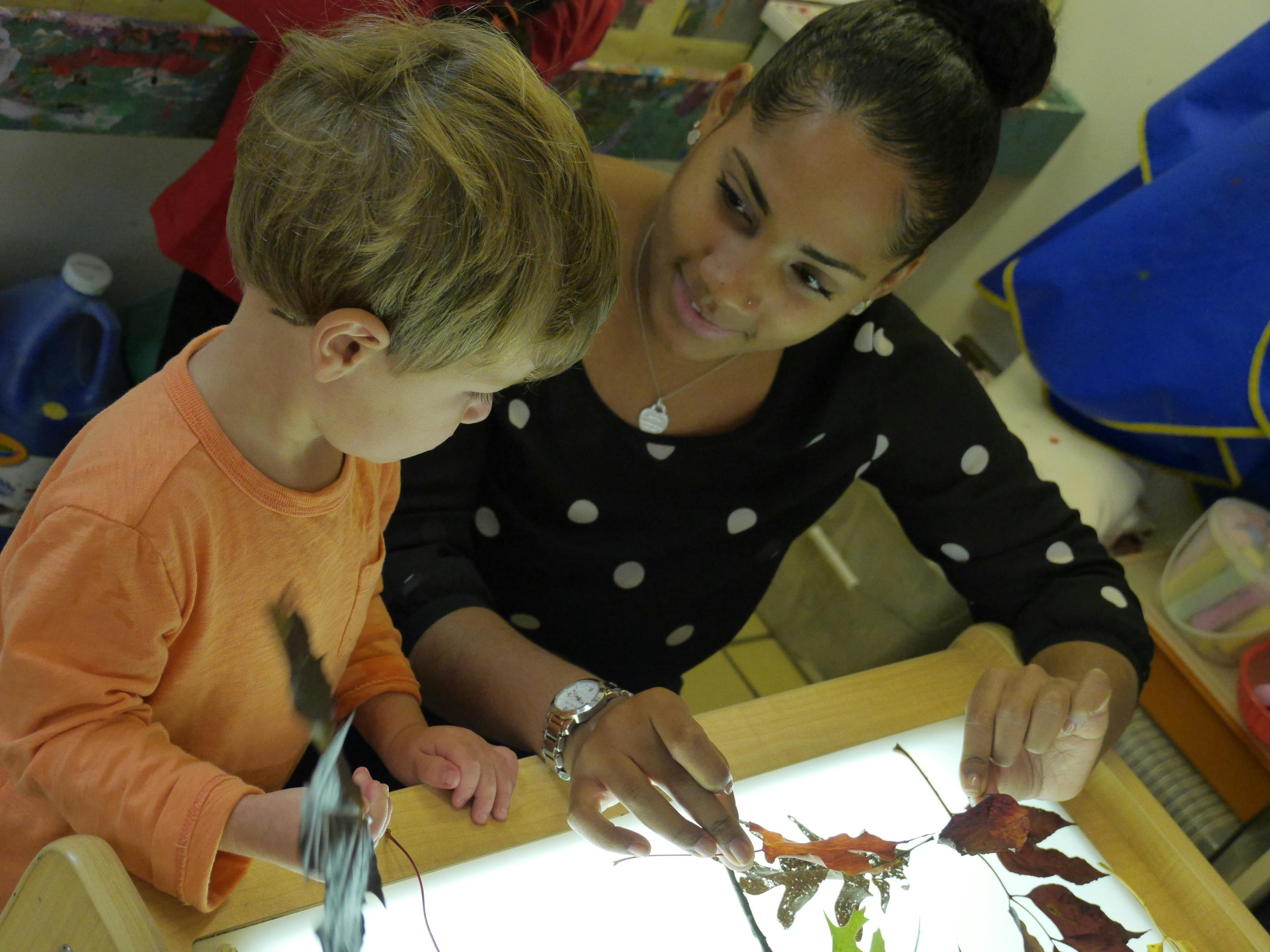 Person and child looking at leaves on a light table