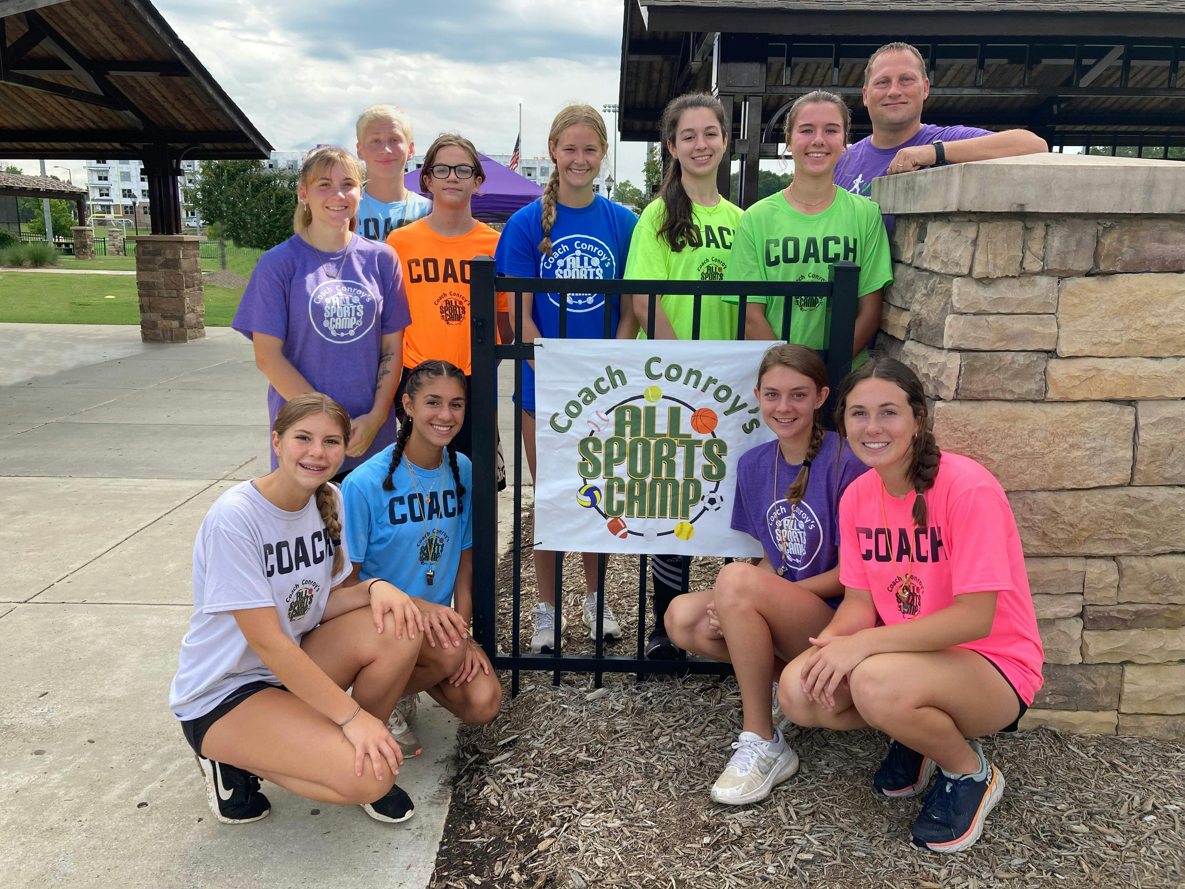 Group of teens and adults posing with a banner for "Coach Conroy's All Sports Camp"