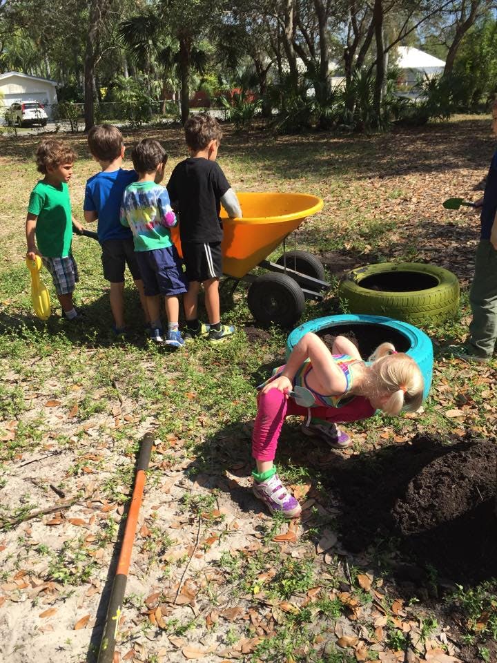 Children playing outdoors with a wheelbarrow and tires