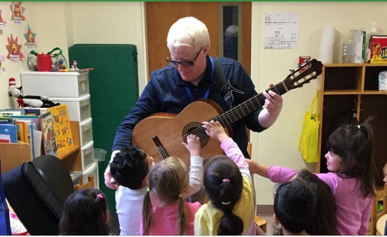 Person playing guitar for a group of children in a classroom