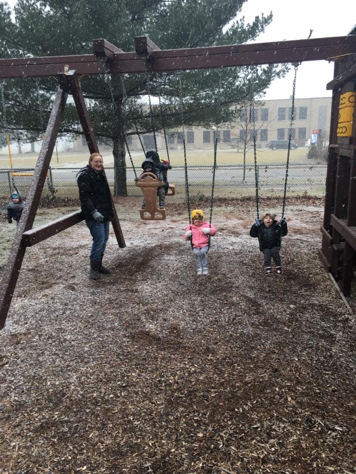 Person standing near children on swings at a playground