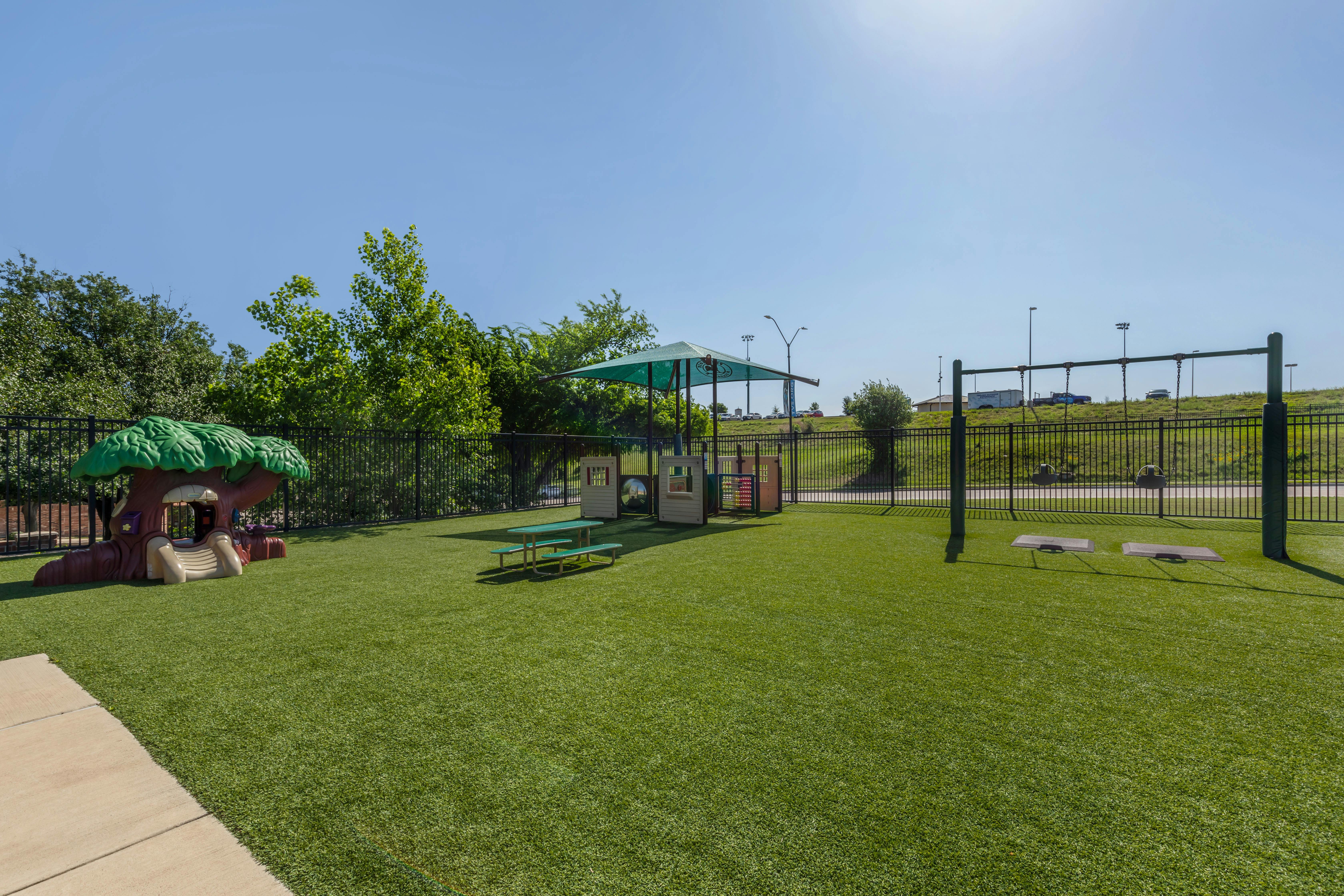 Playground with swings, a playhouse, and a tree-shaped climbing structure on artificial turf