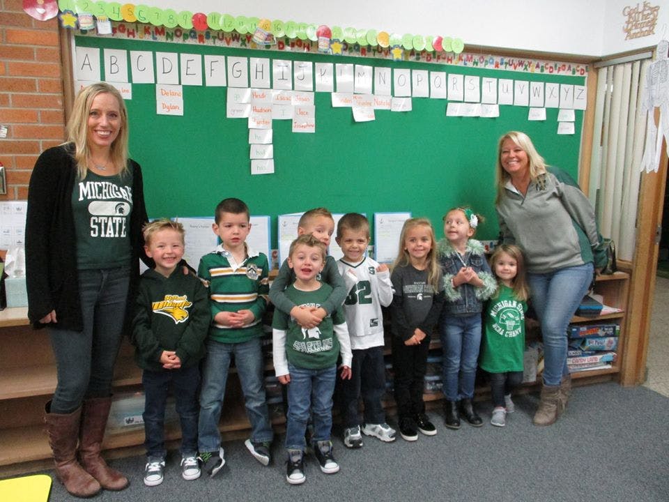 Two adults and a group of children standing in a classroom