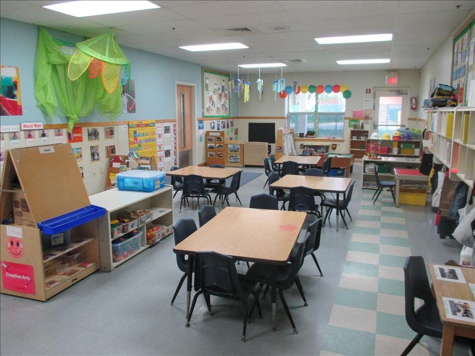 Empty classroom with small tables and chairs, shelving, and decorations