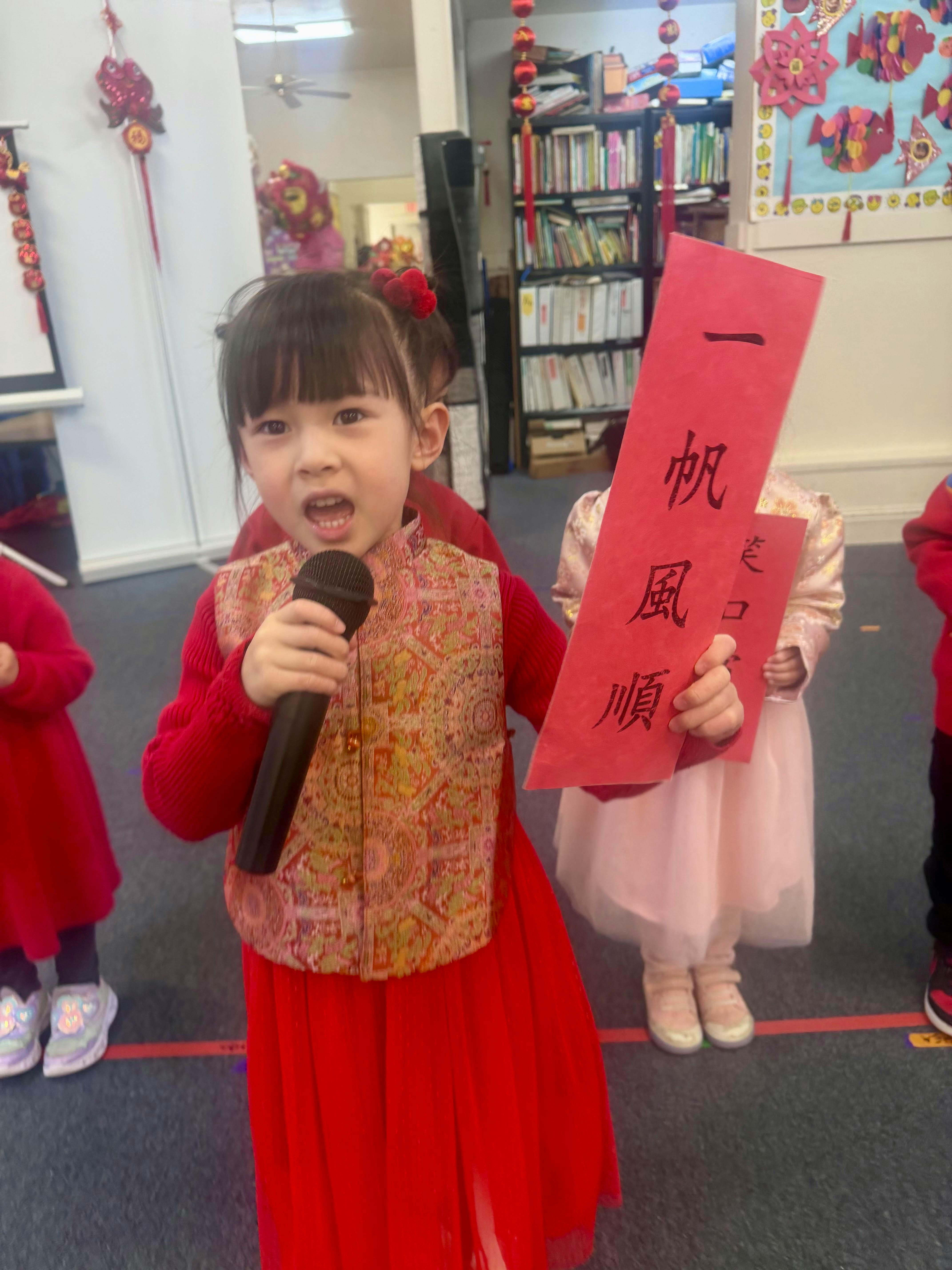 Child speaking into a microphone while holding a red banner with Chinese text