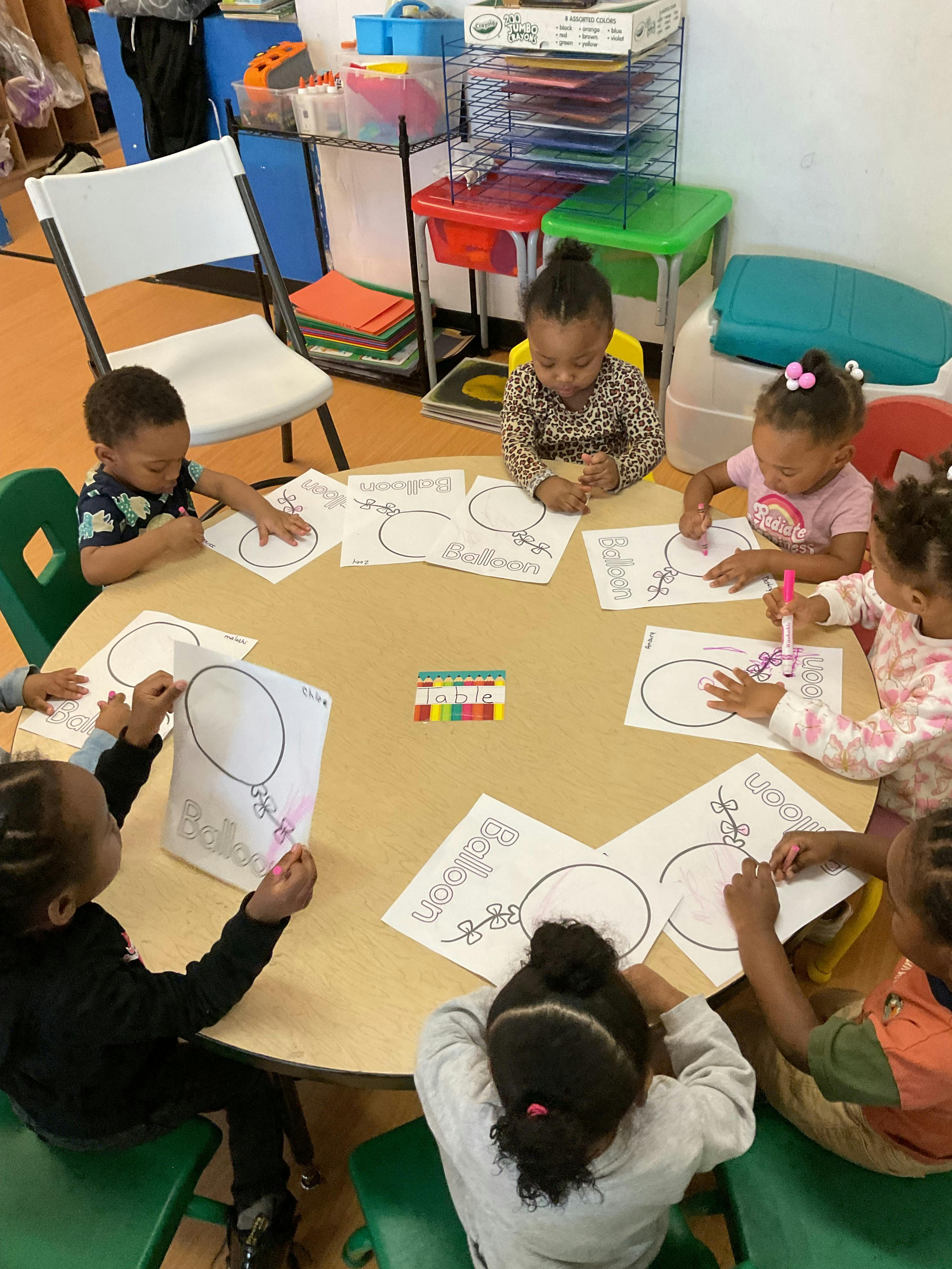 Children sitting at a table coloring balloon pictures