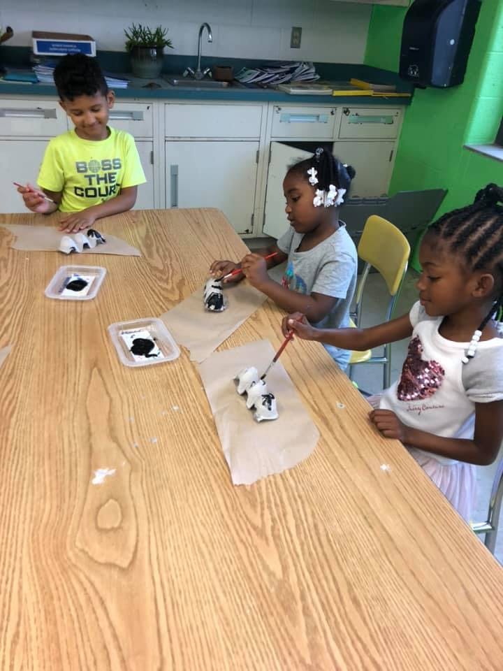 Three children painting small figurines at a table
