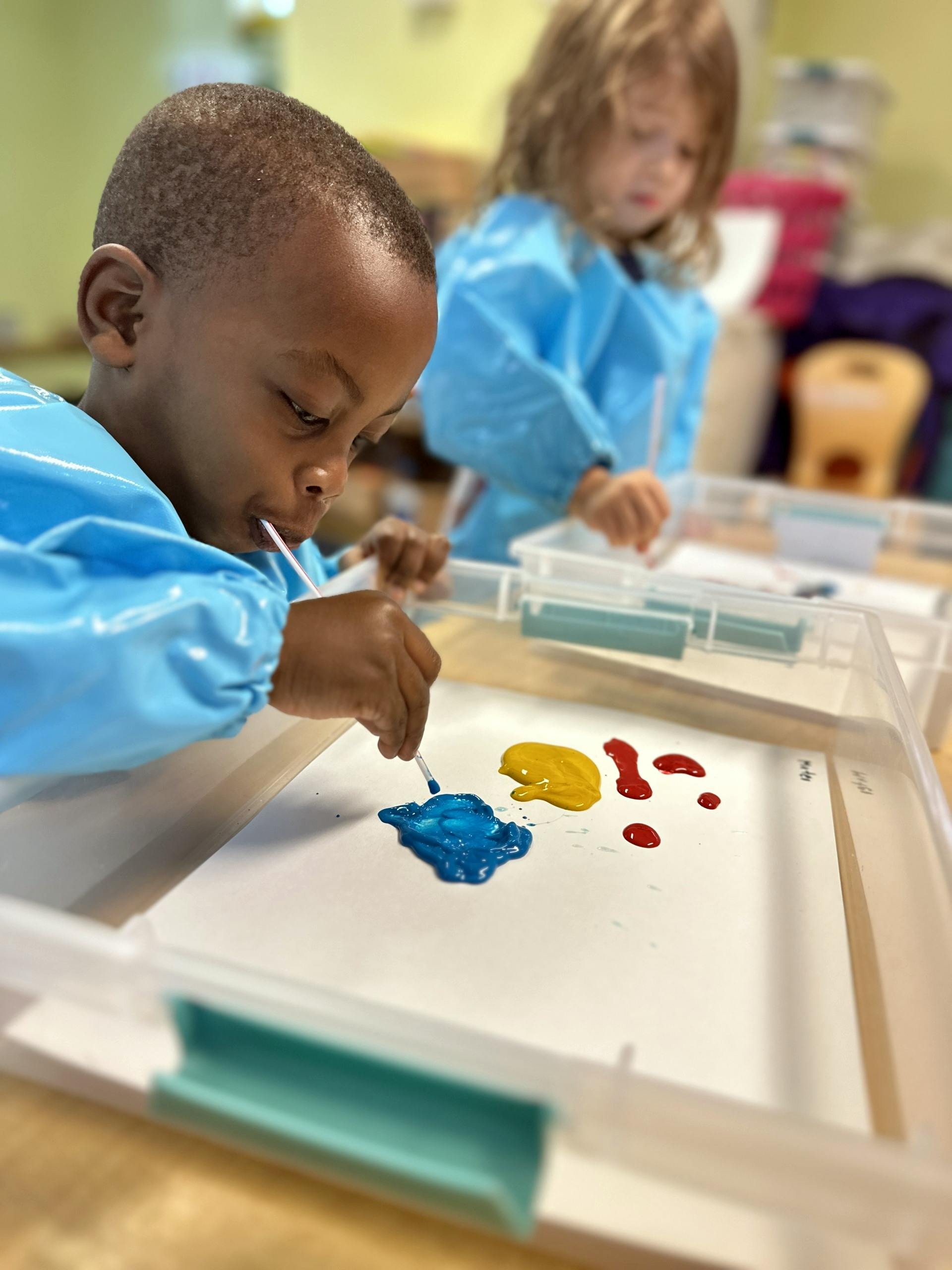 Child in smock painting with blue, yellow, and red paint