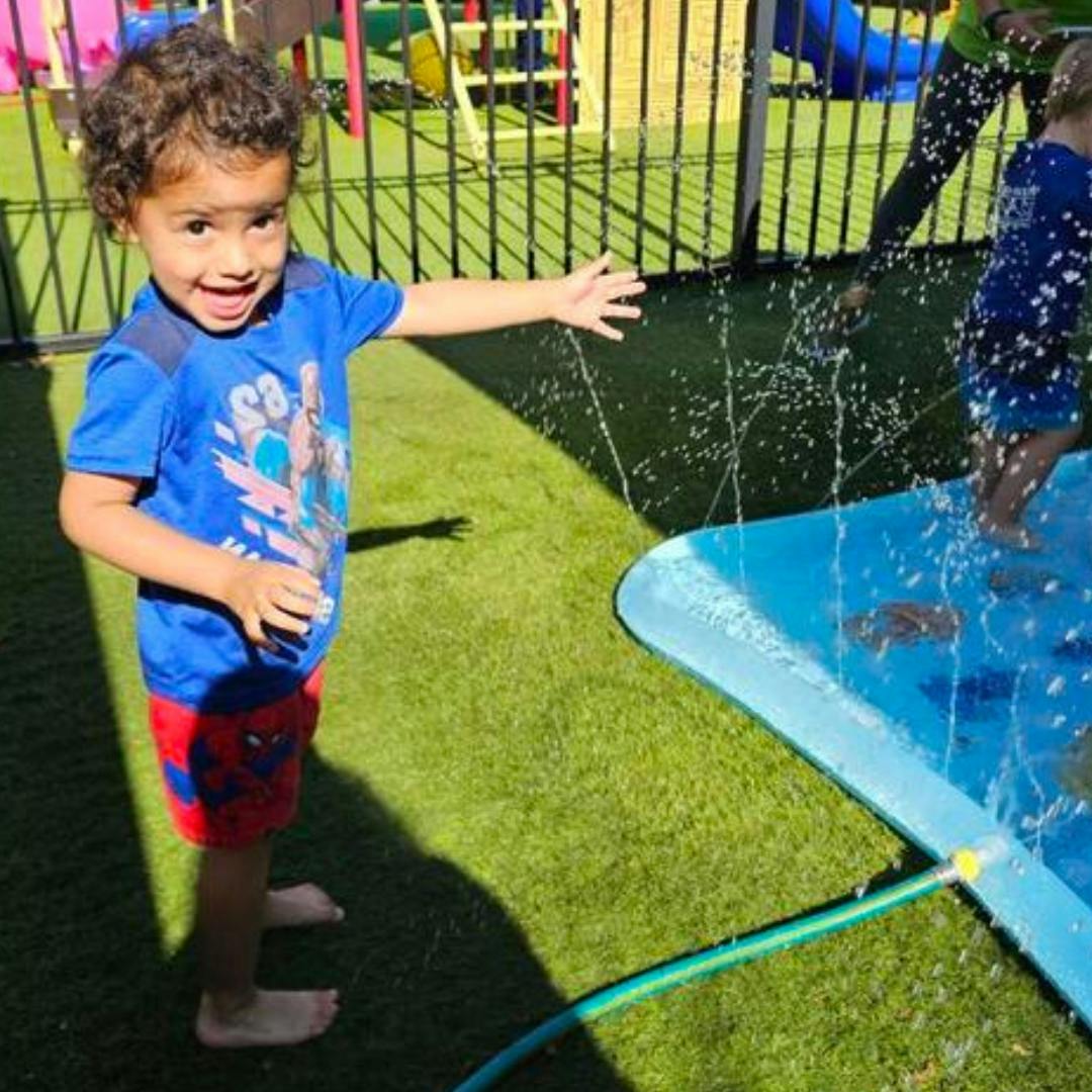 Child playing with water sprinkler on grass