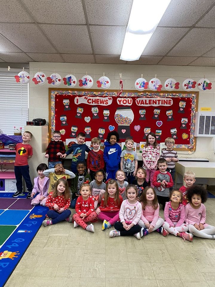 Group of children posing in a classroom with a "I CHEWS YOU VALENTINE" sign