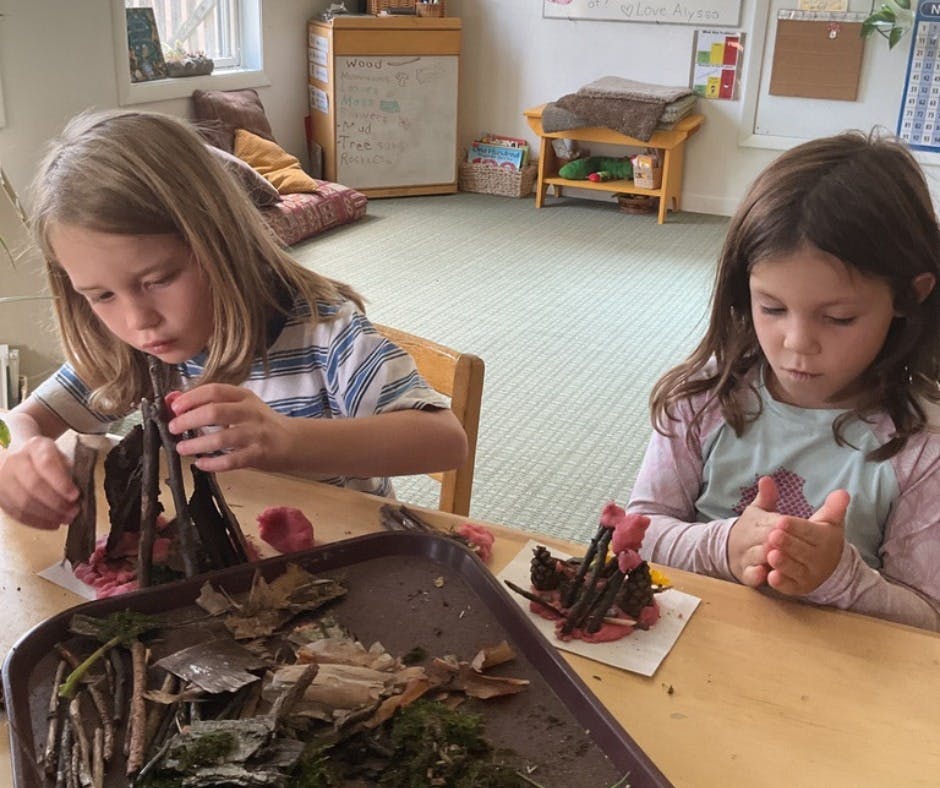 Two children making crafts with natural materials at a table