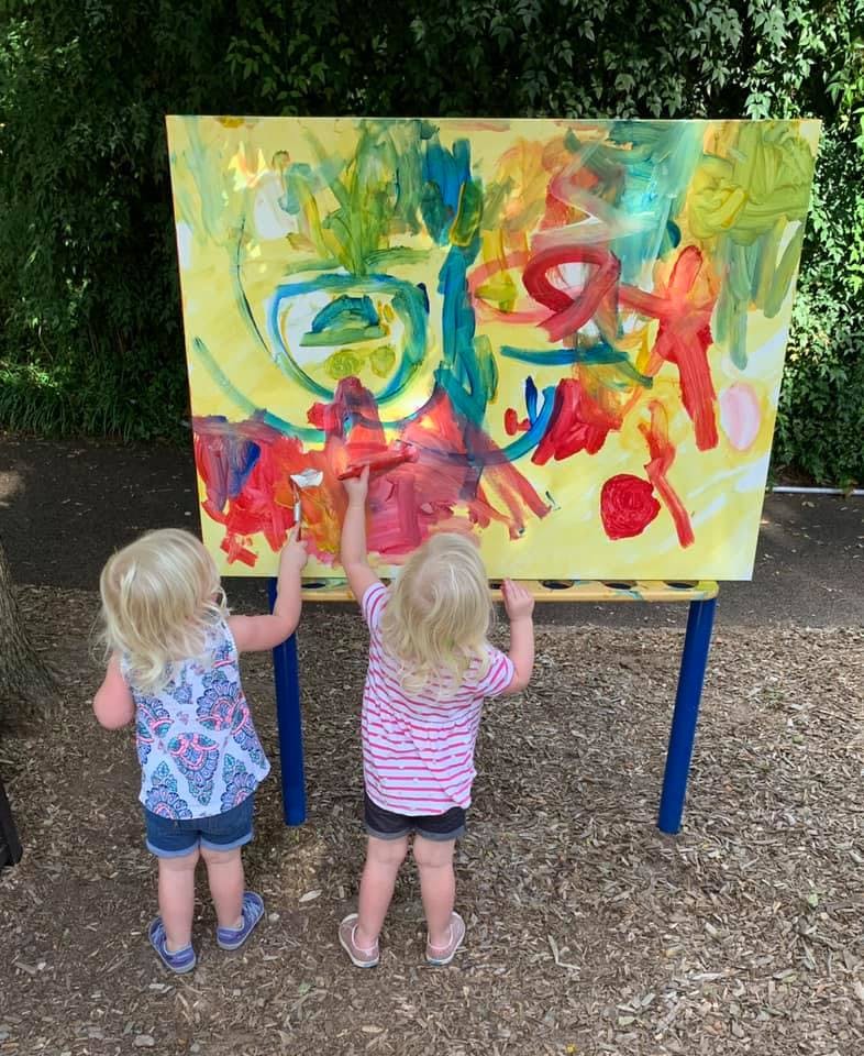 Two children painting on an easel outdoors
