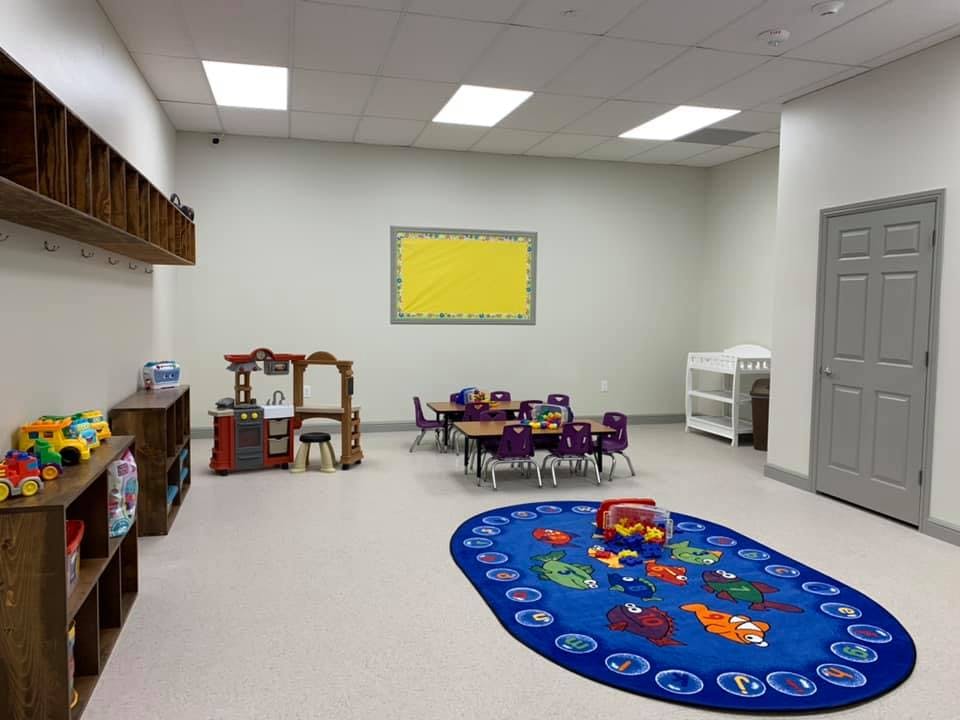 Playroom with small tables and chairs, toy kitchen, and blue rug