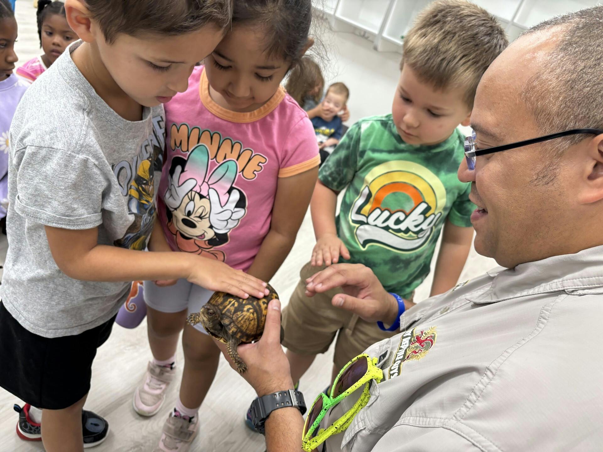 Adult holding a turtle while children touch its shell