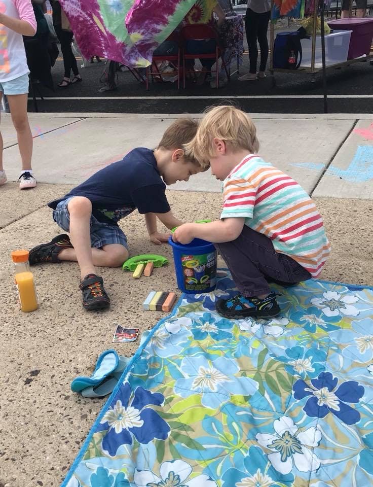 Two children playing with a bucket and chalk on a blanket outdoors