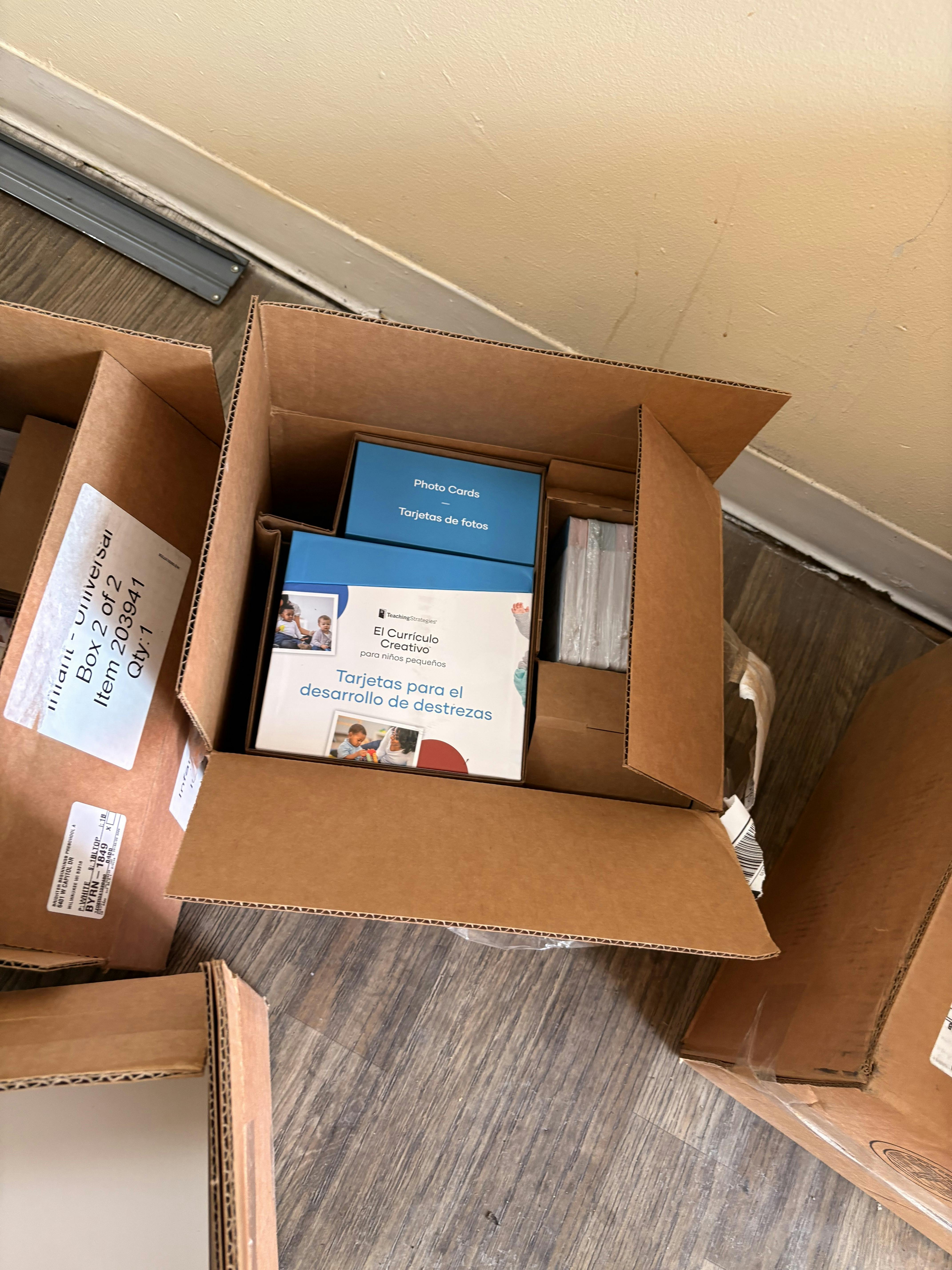 Open cardboard box containing "Photo Cards" and "El Currículo Creativo" materials