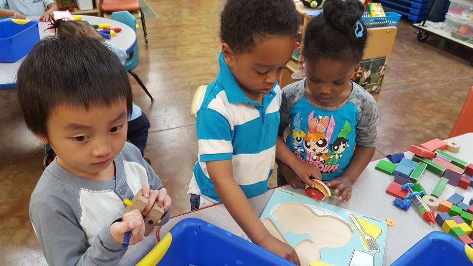 Three children playing with puzzles and blocks at a table