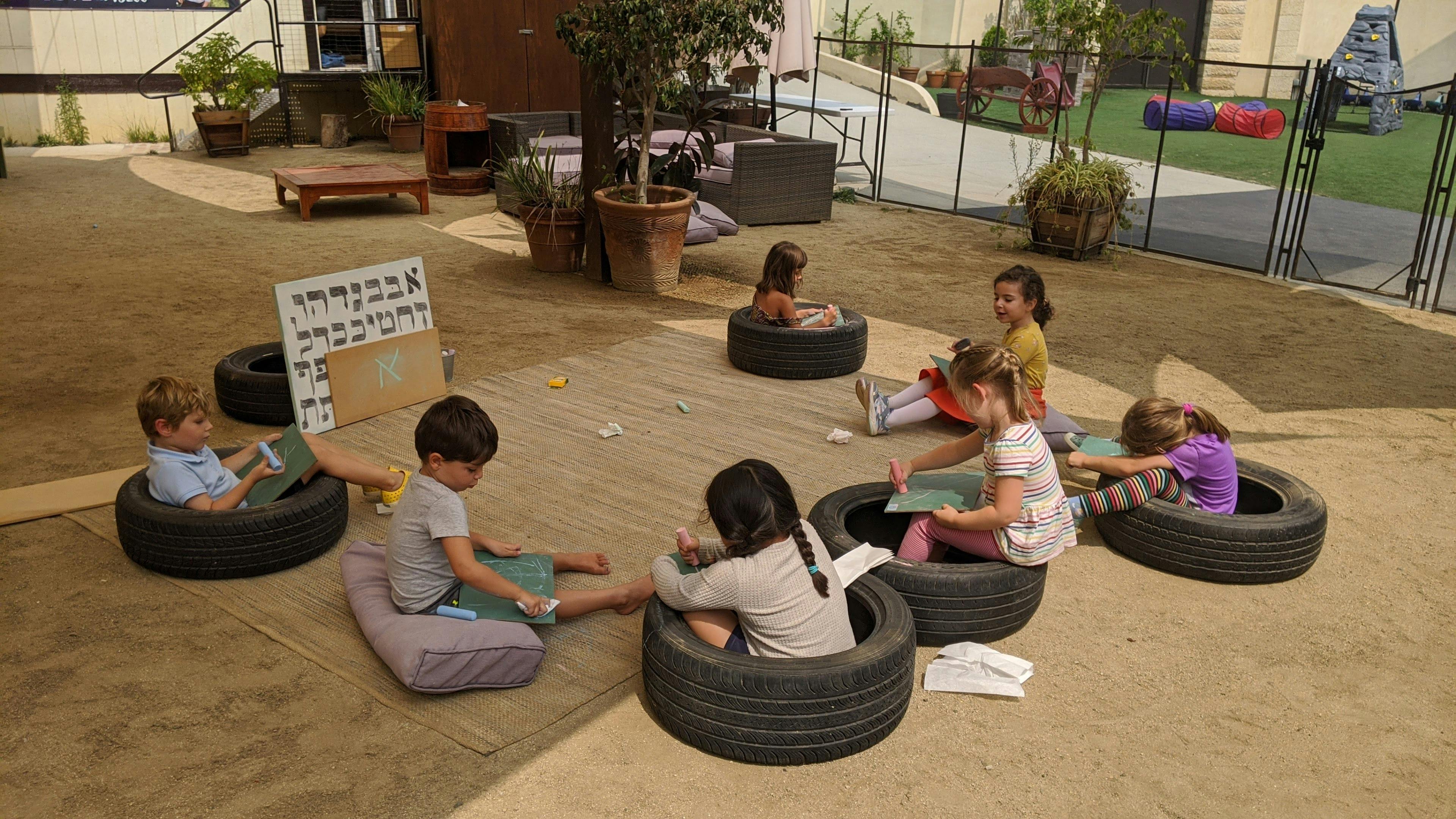 Children sitting in tires and on cushions in an outdoor classroom