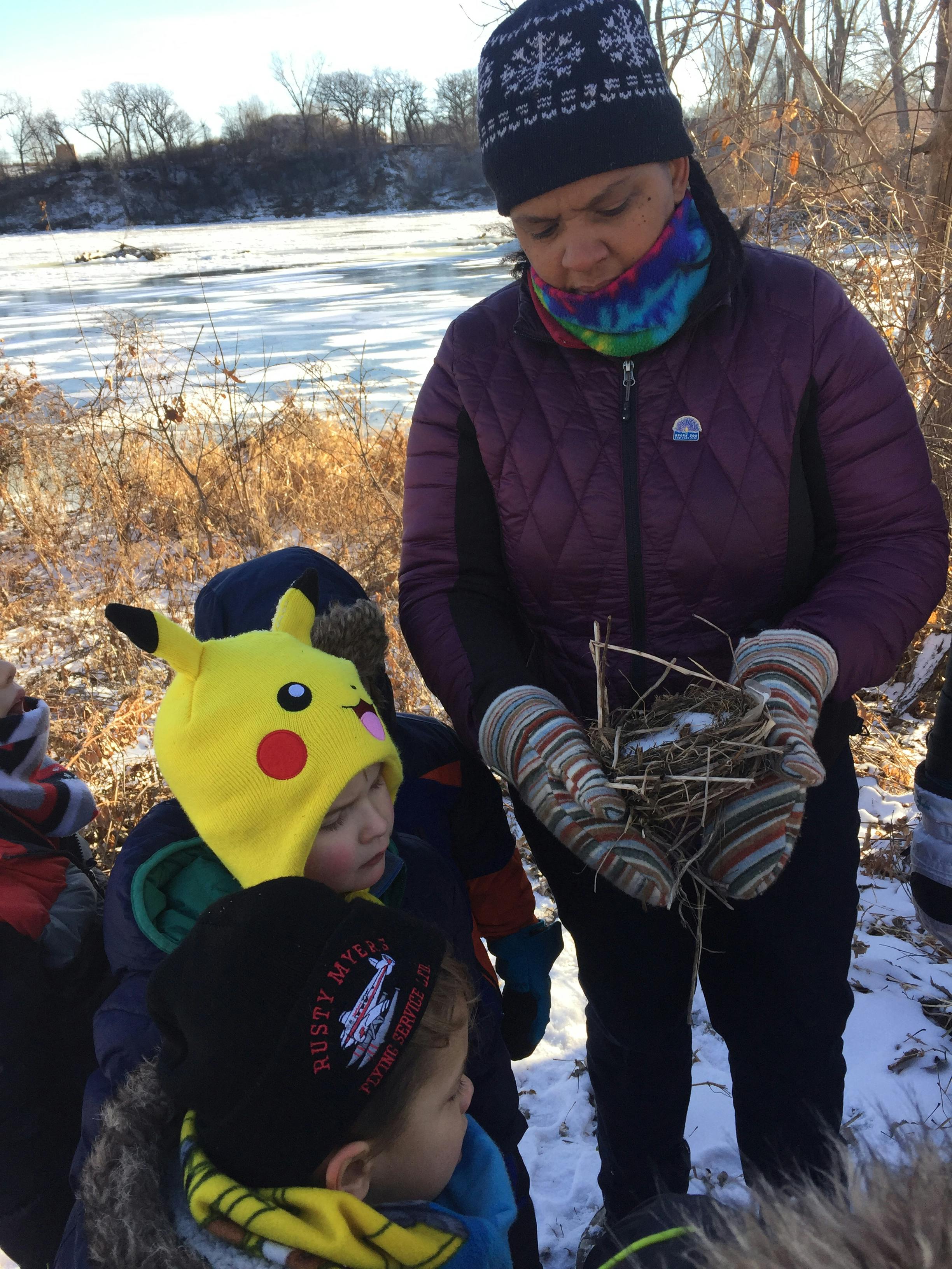 Person in mittens holding a bird's nest, surrounded by children