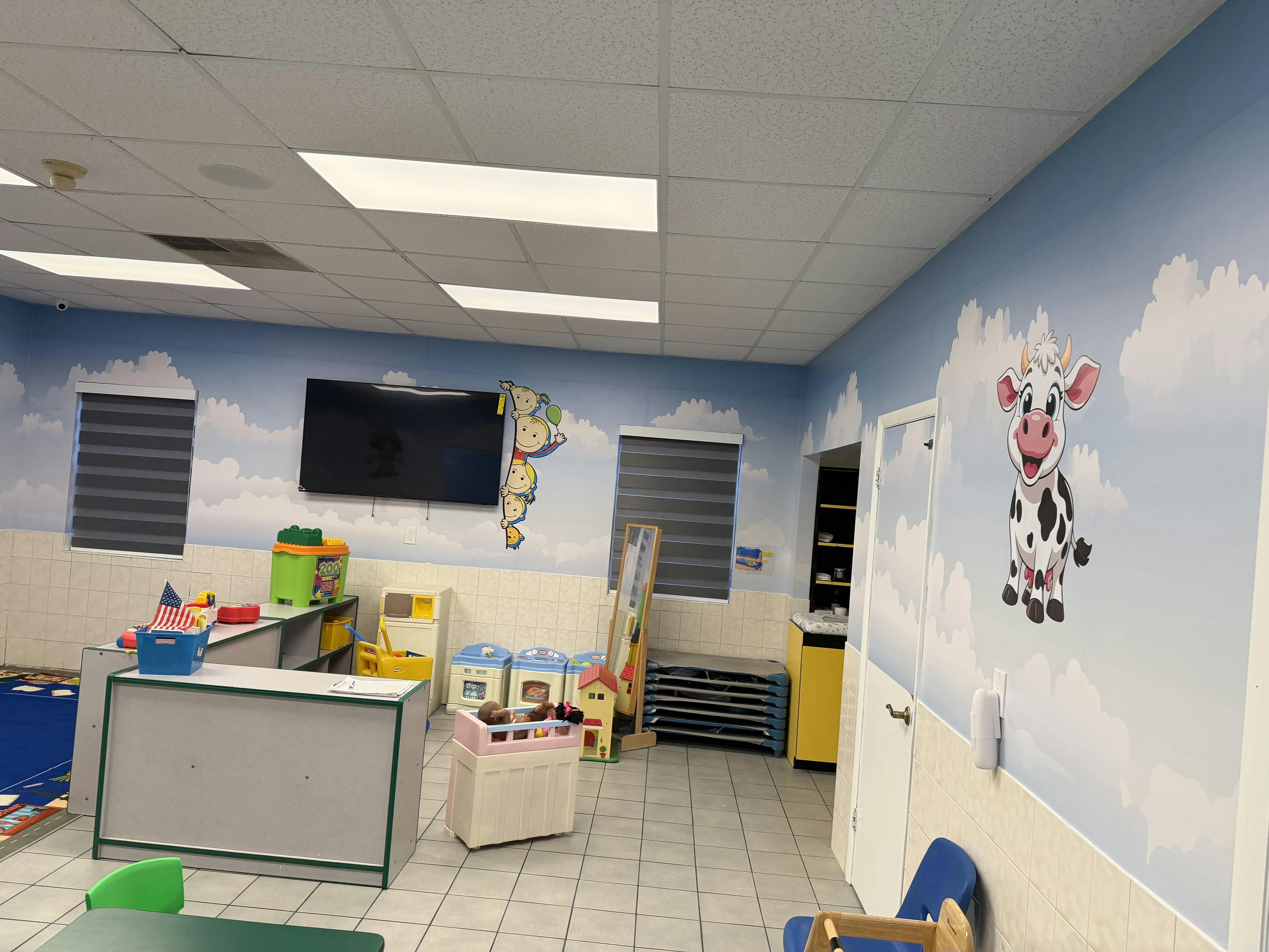 An empty classroom with blue and white cloud-painted walls, play kitchen, and toys