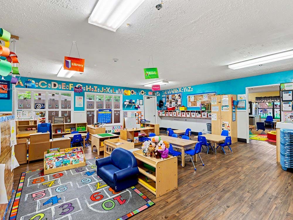 An empty children's classroom with small tables, chairs, and learning materials