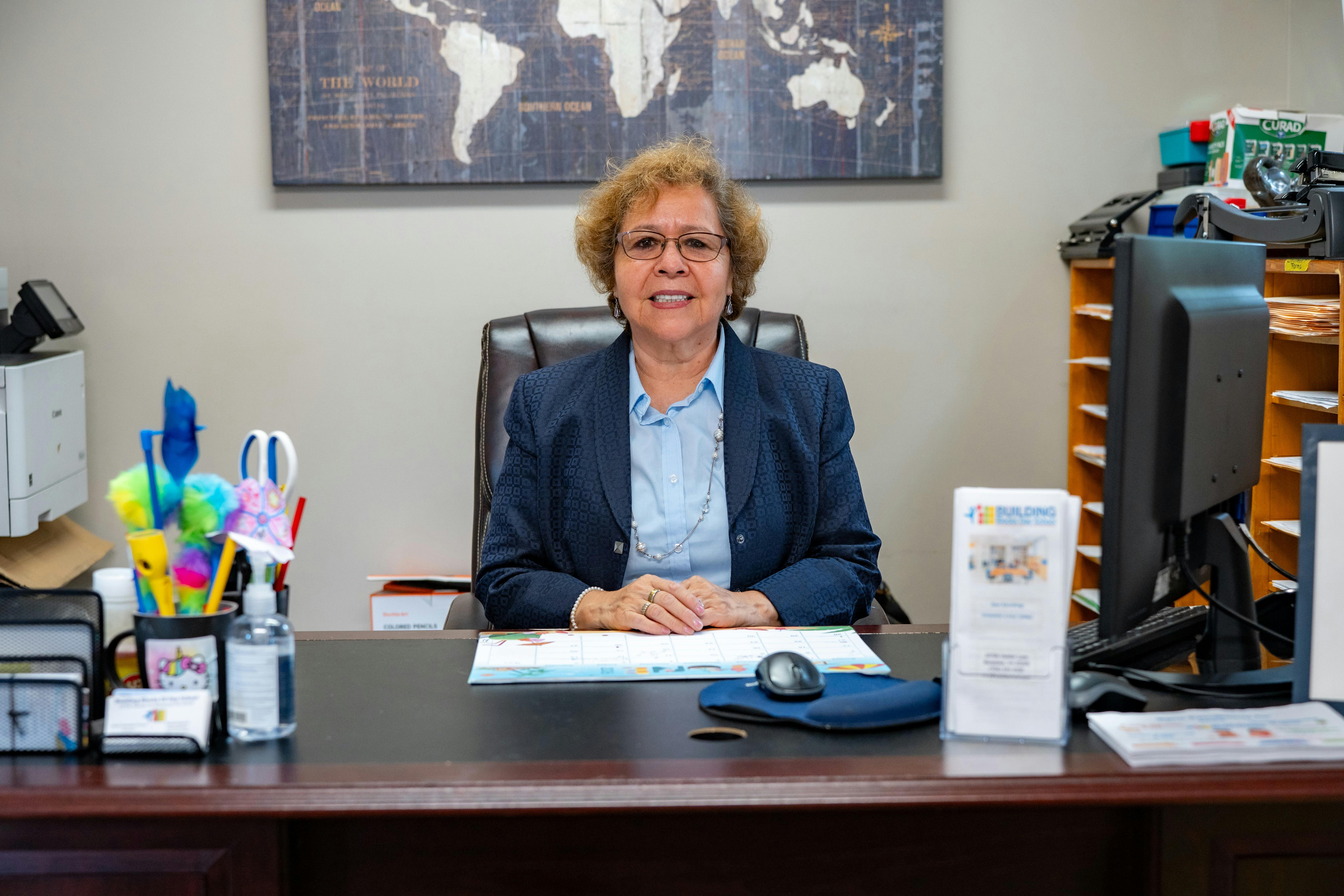 A person sitting at an office desk with a world map on the wall behind them