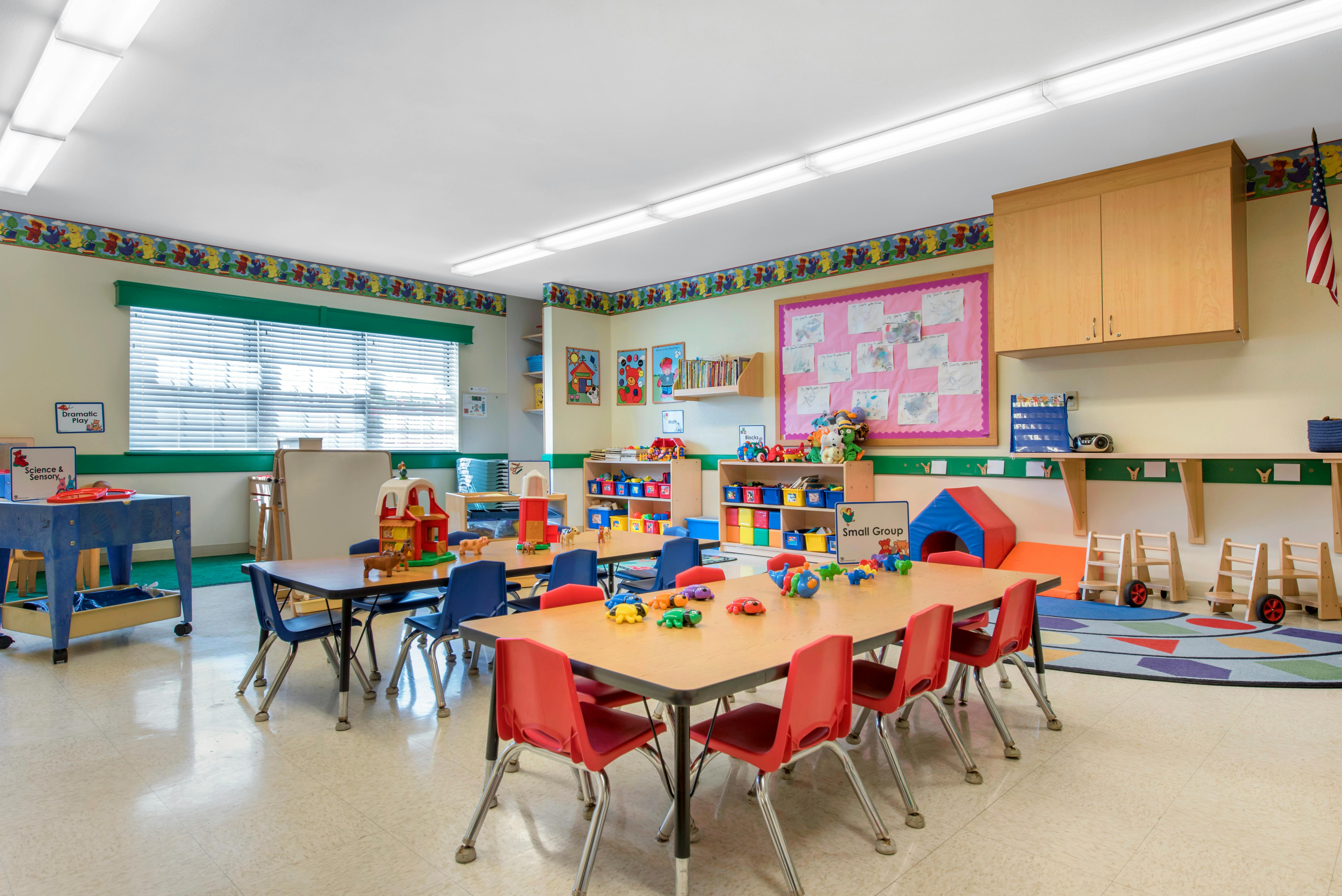 Classroom with small tables and chairs, shelves with toys, and posters on the walls