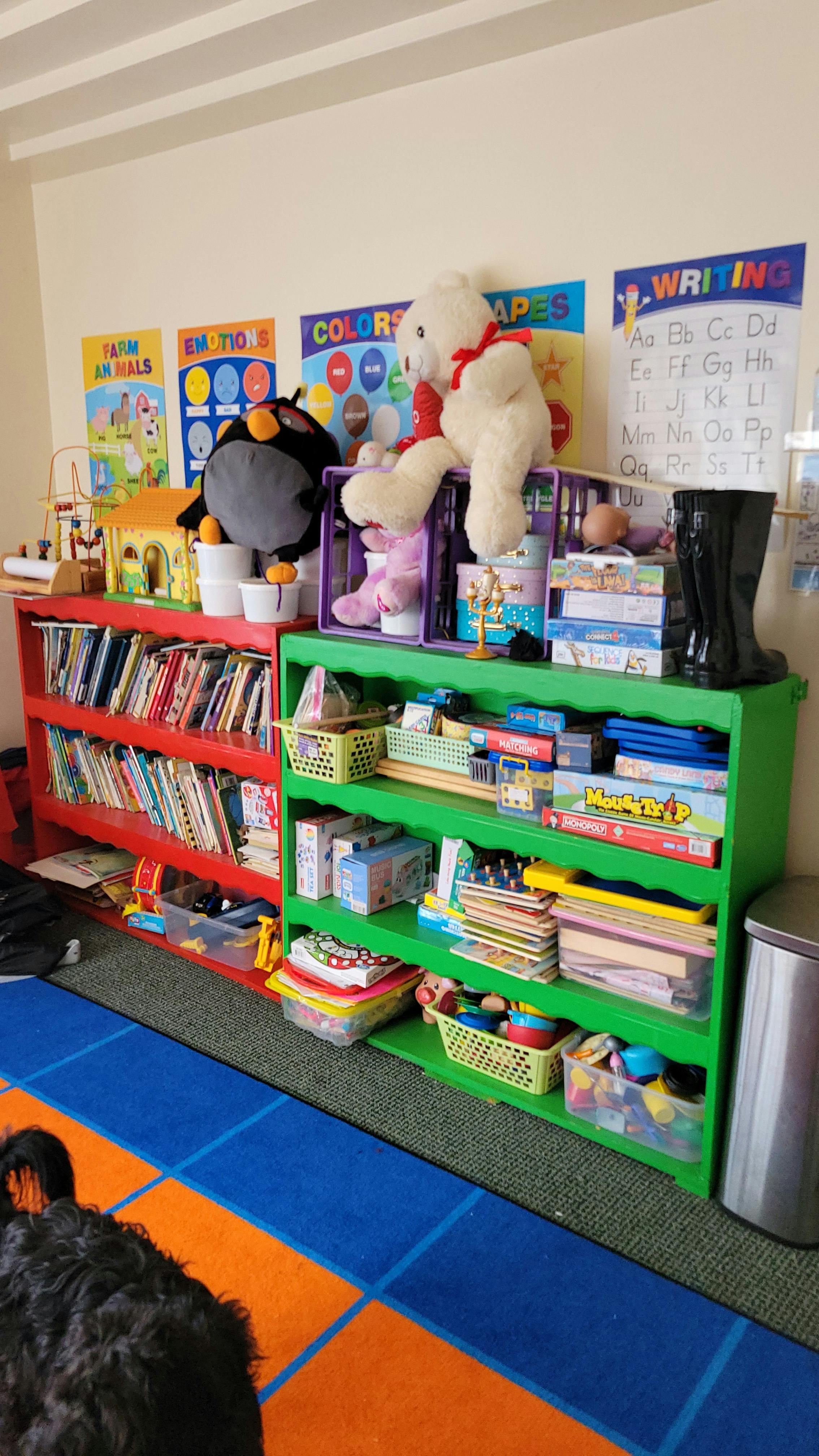 Red and green bookshelves filled with books and toys in a classroom