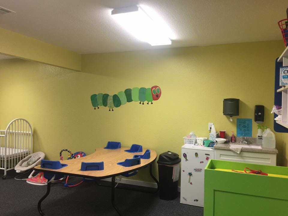 Playroom with a crib, table with blue seats, and a caterpillar wall decal