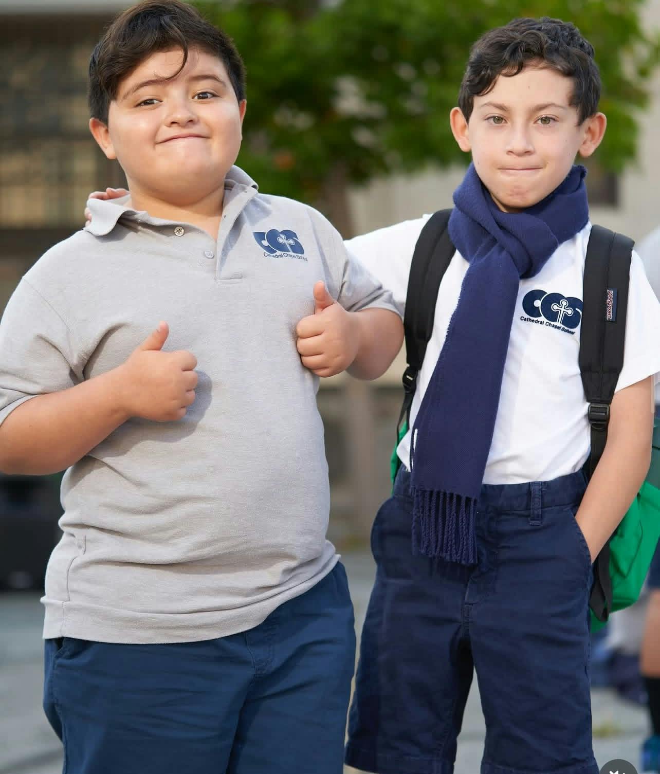 Two children in school uniforms, one giving thumbs up