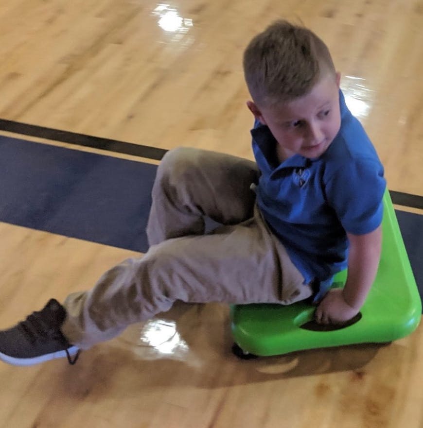 Child sitting on a green scooter board on a wooden floor