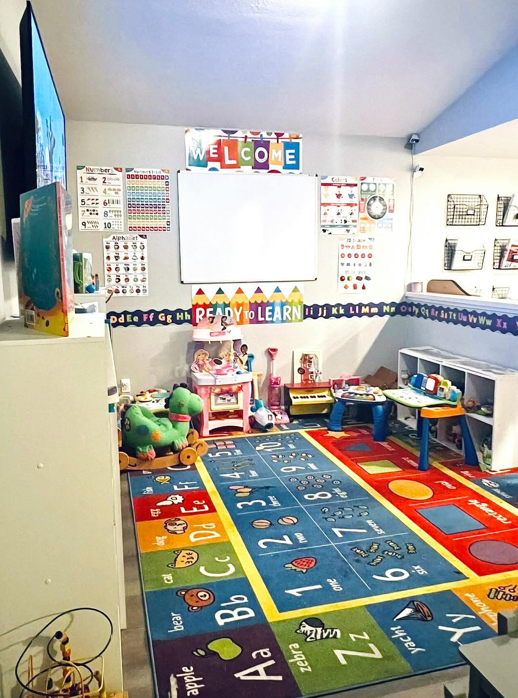 Playroom with a colorful alphabet and numbers rug, toys, and a whiteboard with "WELCOME"