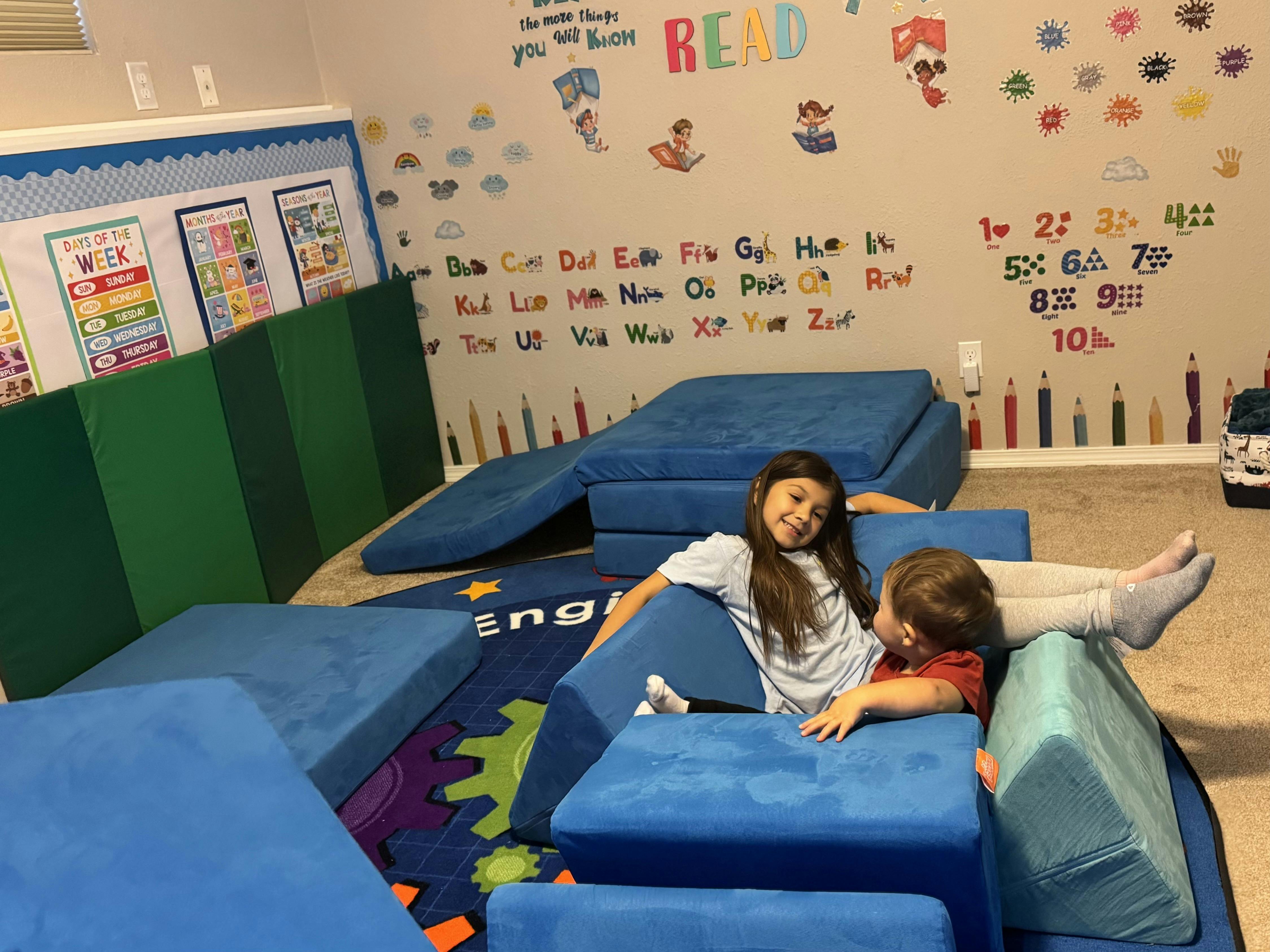 A teen and a child sitting on blue foam play mats in a classroom