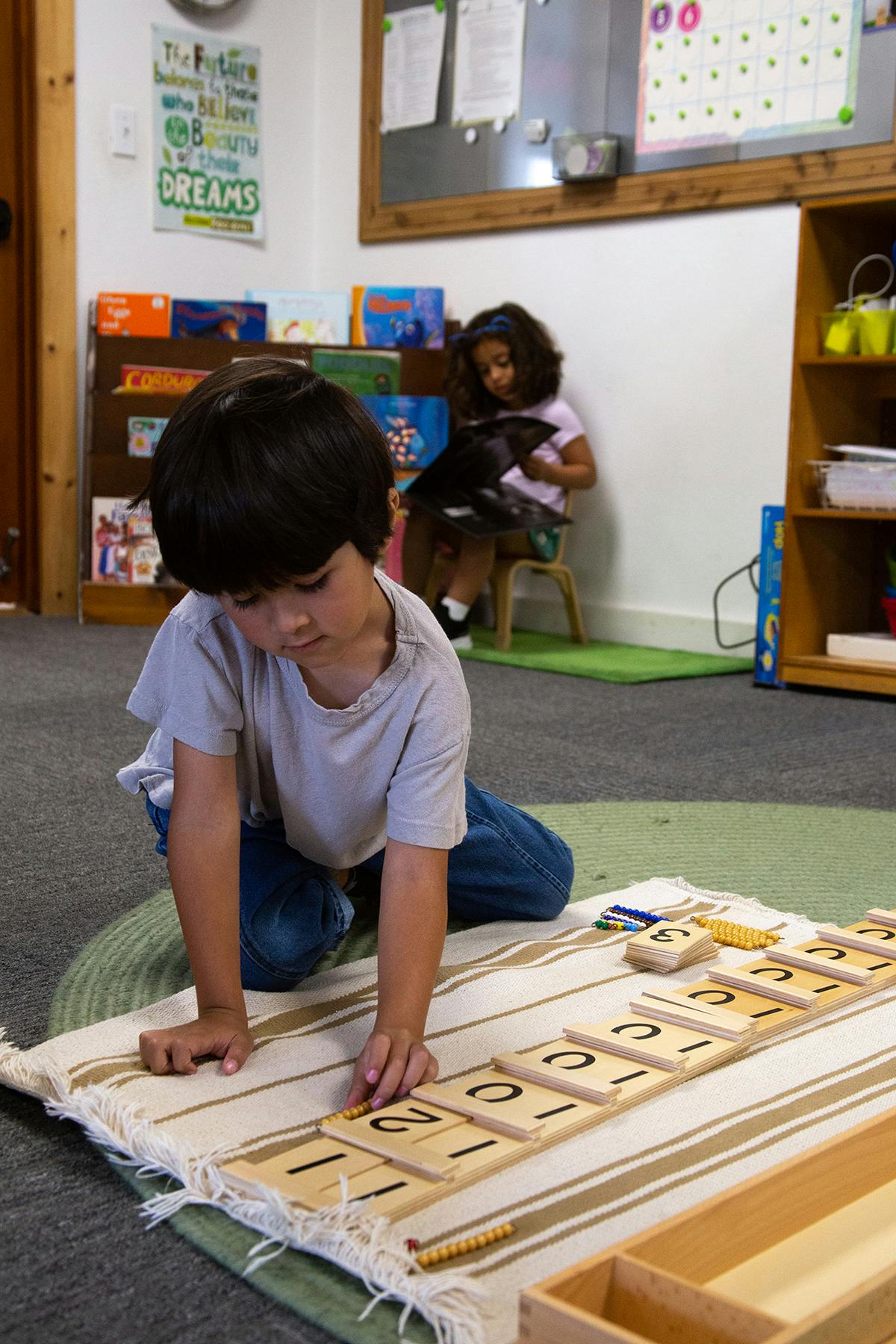 Child kneeling on floor, arranging number tiles on a mat